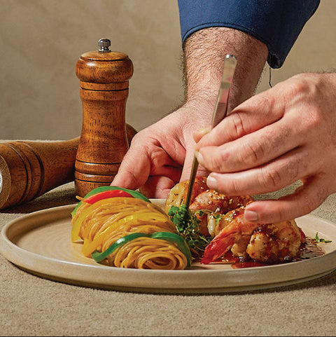Person cutting into a dish of pasta with a fork and knife on a beige plate.